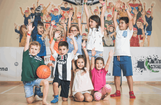 Bambini in spazio gioco con le braccia alzate.