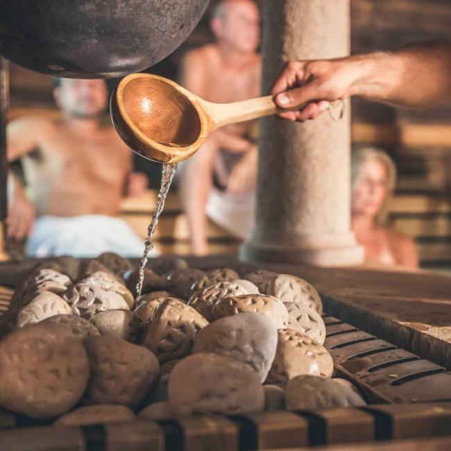 Hand with ladle pouring water onto the sauna steamer.