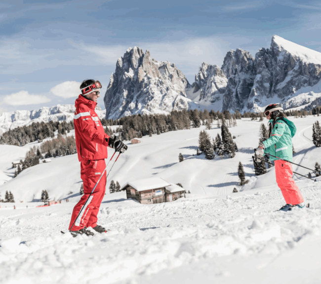 Bambina scia con istruttore fuori dal family hotel in montagna.