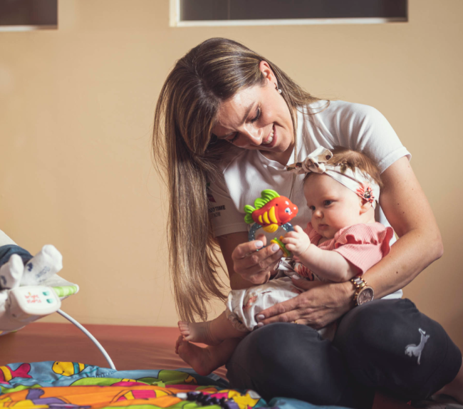 Mamma con bimba piccola in braccio che gioca con un pesciolino finto.