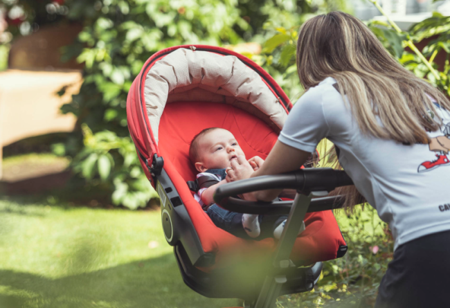 Neonato dentro al passeggino sorride alla mamma.