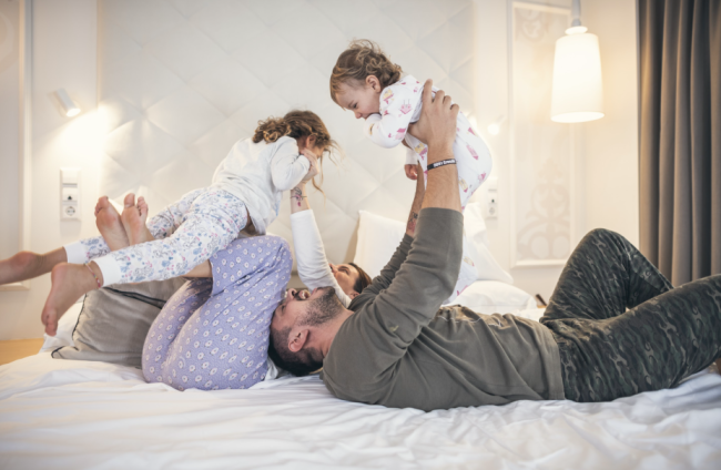 Famiglia felice gioca sul letto in stanza d'hotel.