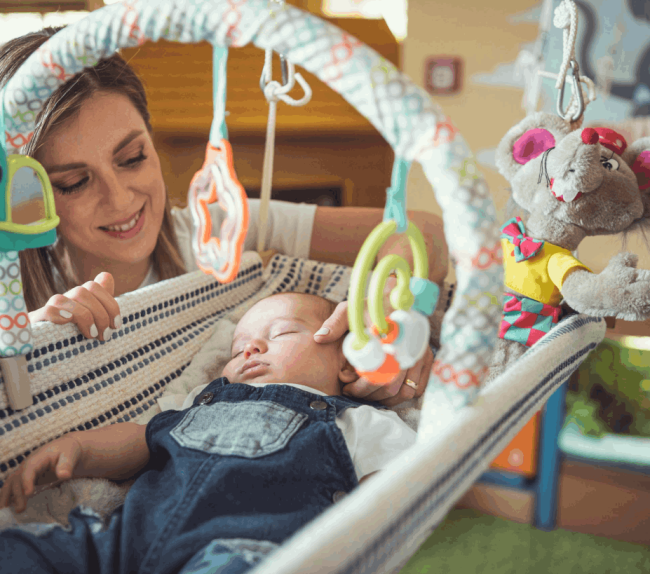 Bimbo neonato dorme in culla mentre l'educatrice lo guarda sorridente.