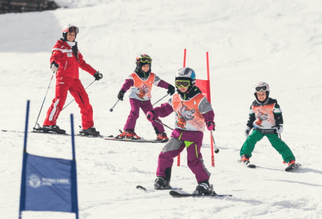 Bimbi in pista da sci che imparano a sciare col maestro che li segue.
