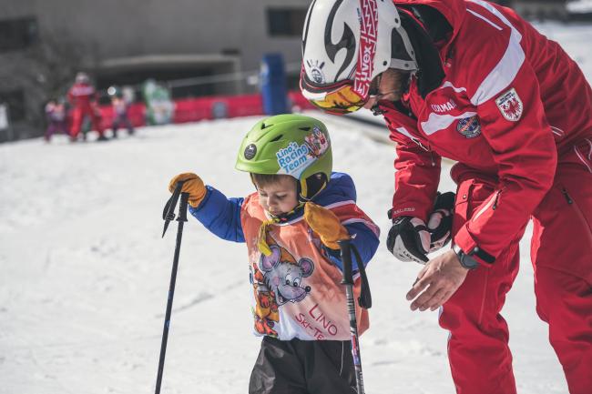 Bimbo che scia sulla neve aiutato dal maestro.