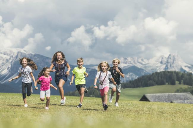 Kinder laufen über die Wiese in den Bergen - ferien mit kindern Südtirol