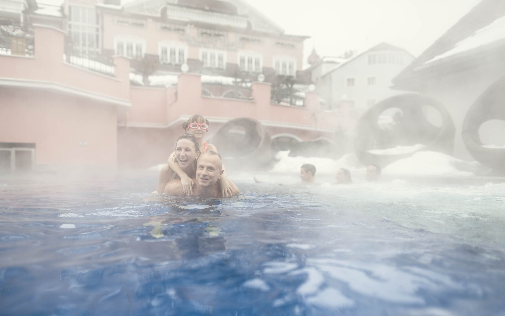 Padre, madre e figlio giocano nell'acqua del family hotel in Val Gardena con piscine.