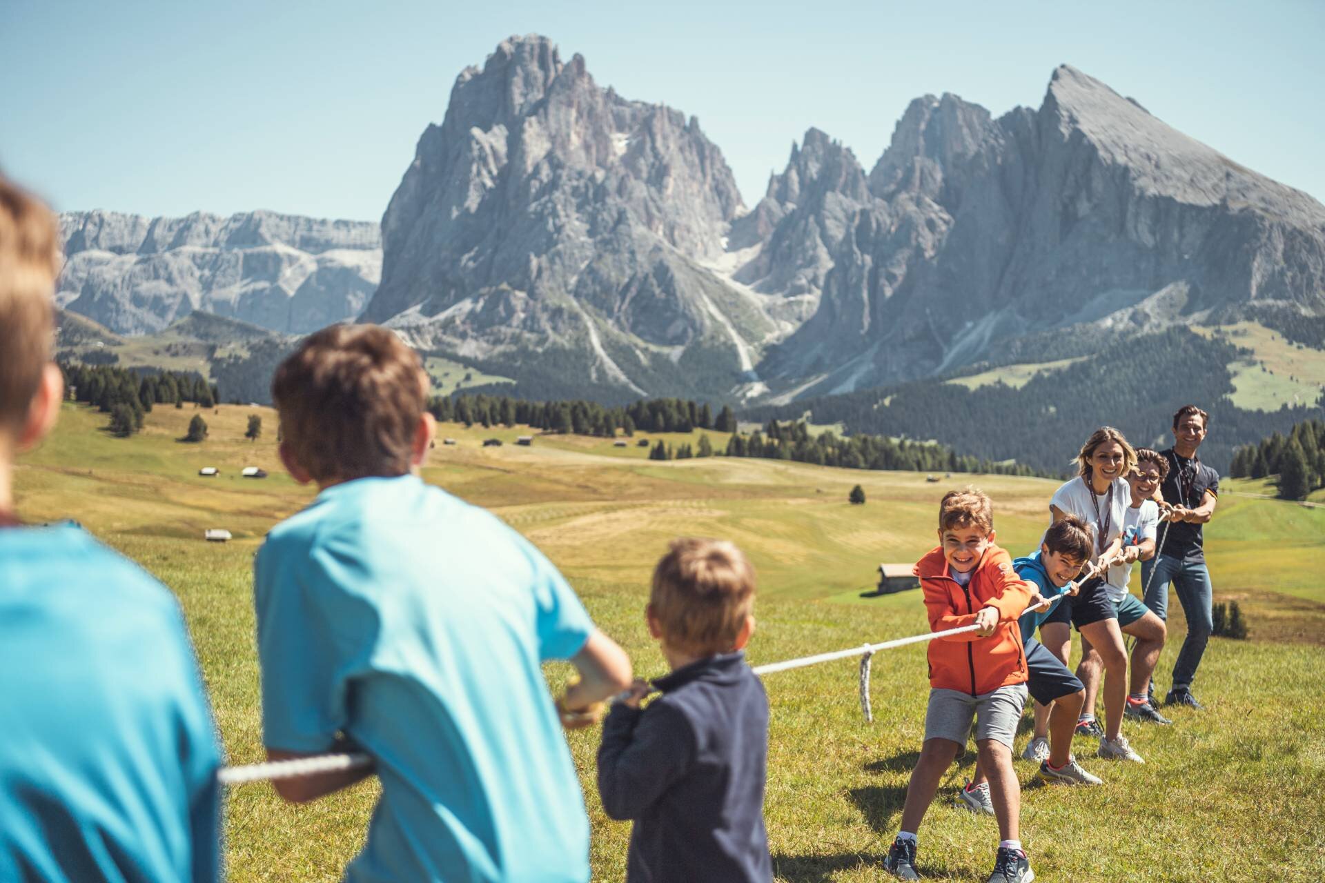 Bambini giocano al tiro alla fune fuori su un prato delle Dolomiti.