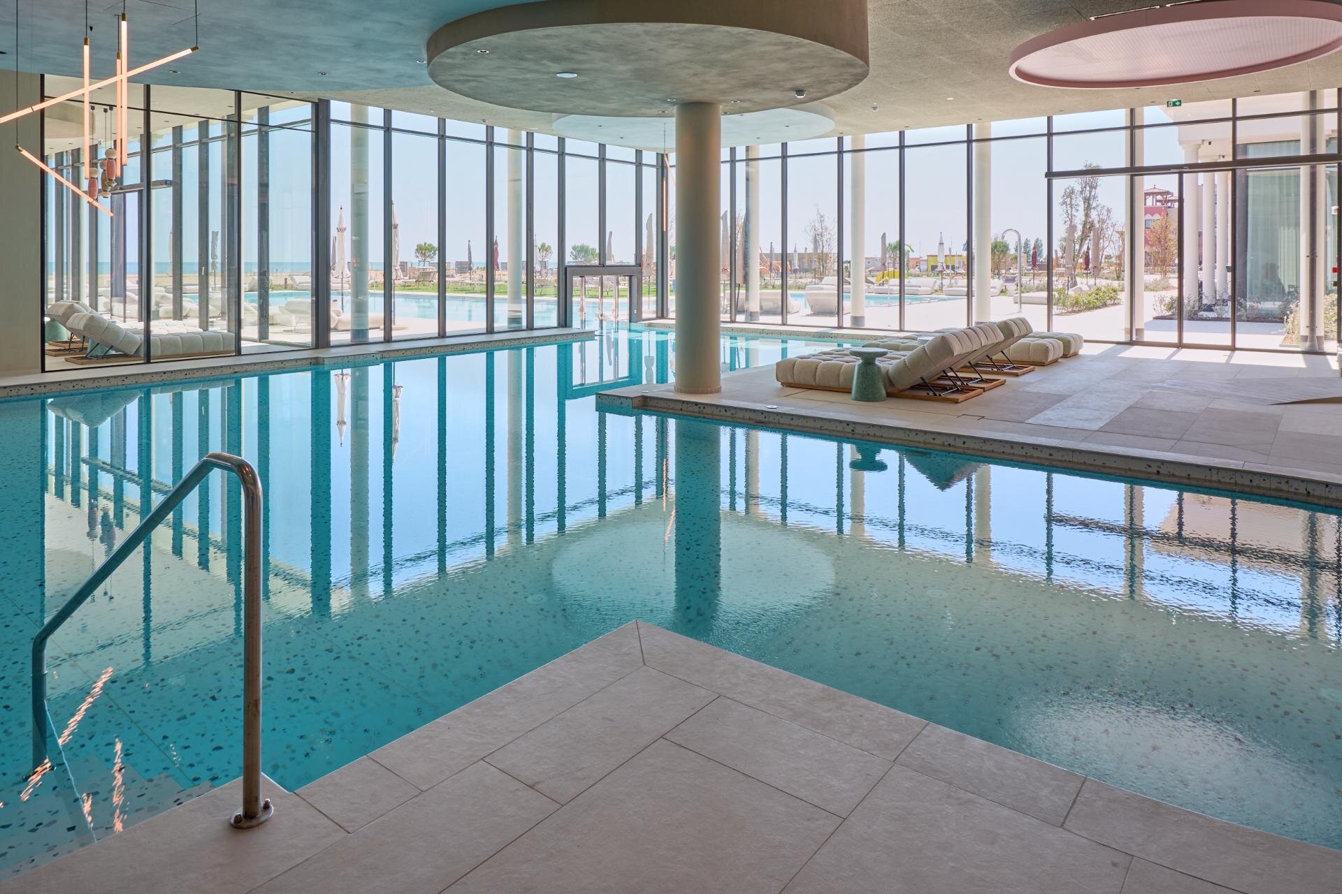 Indoor heated swimming pool interior with a dedicated relaxation area and large panoramic windows in Caorle.