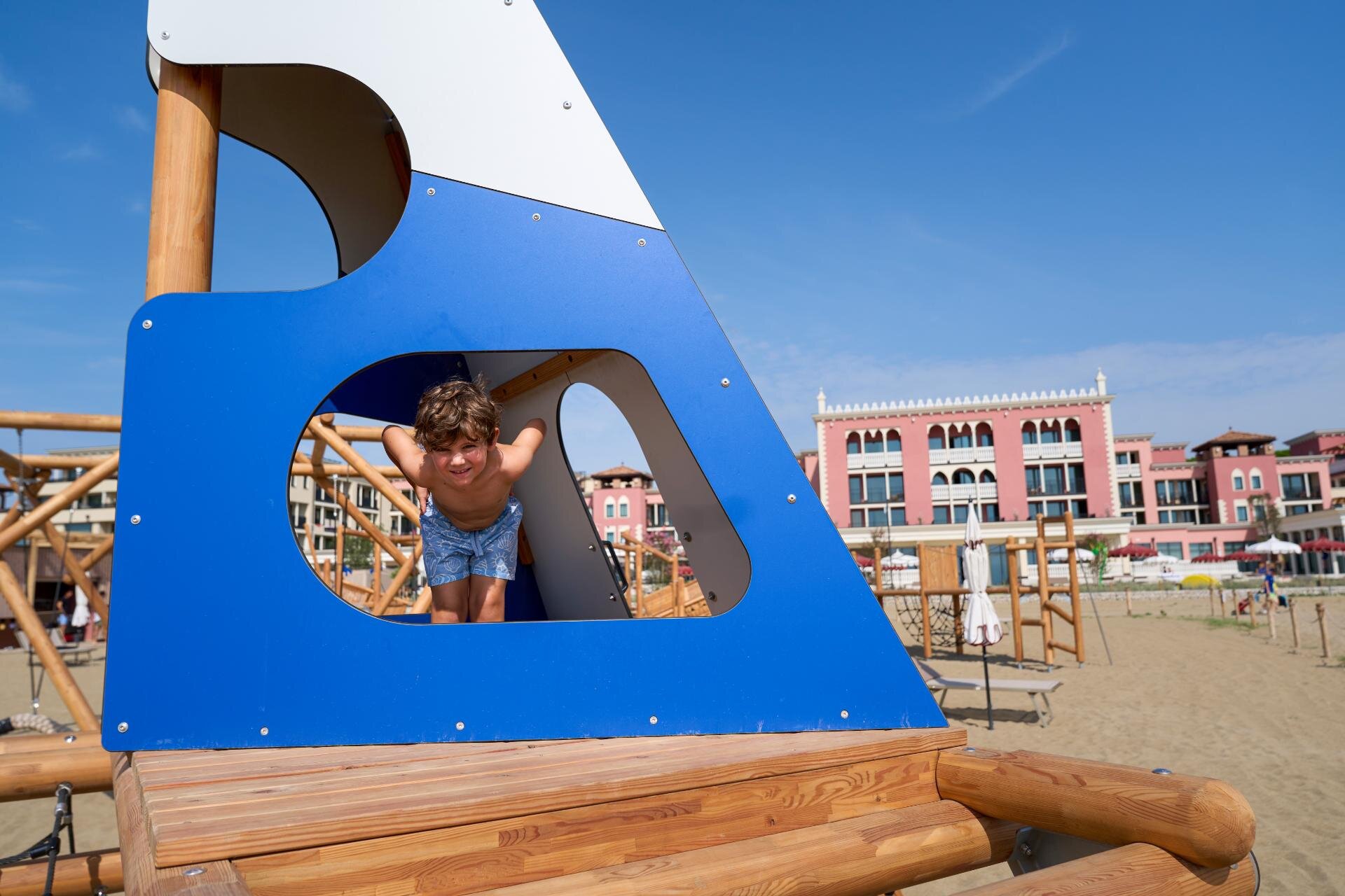 Bambino che si affaccia da una struttura in legno nella spiaggia del Cavallino Bianco a Caorle